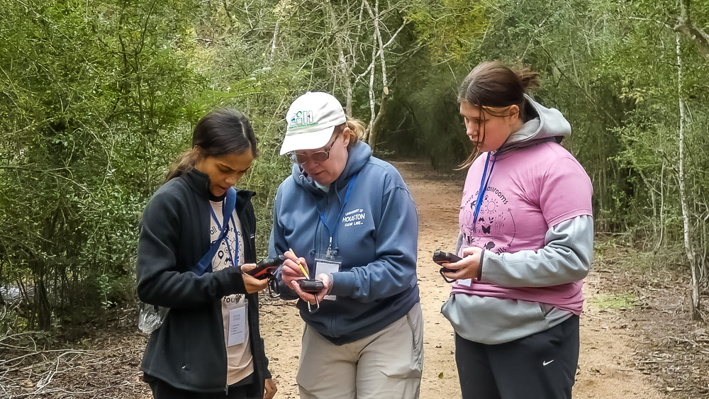 Three people looking at handheld GPS units while on a nature trail.