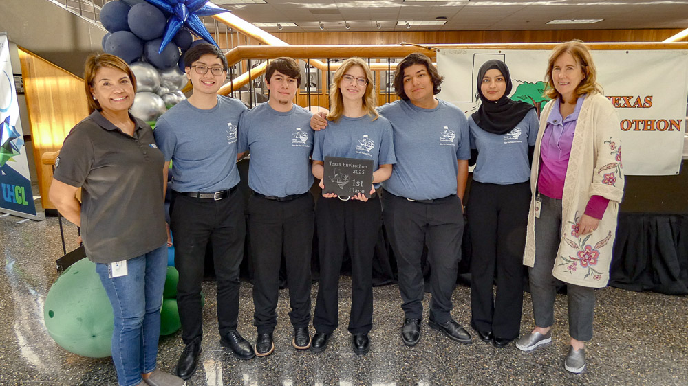 A group of students and professionals pose indoors with a first-place Texas Envirothon plaque.