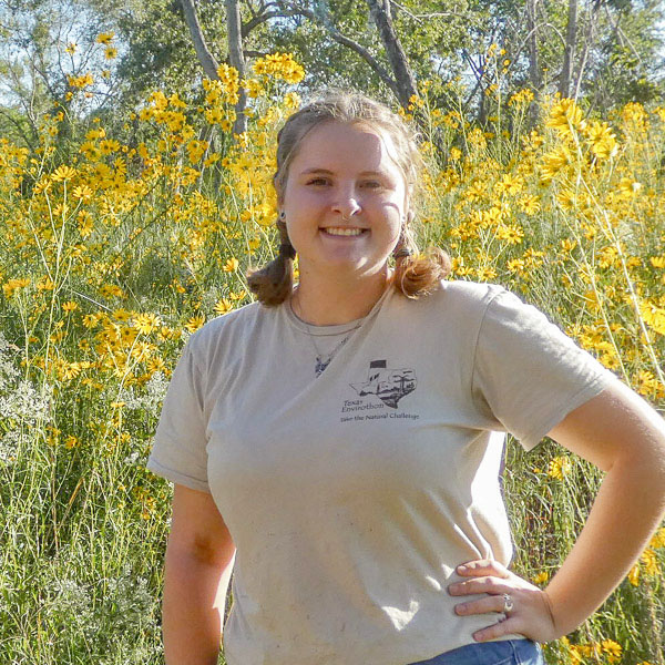 A person stands in front of a field of tall yellow flowers.