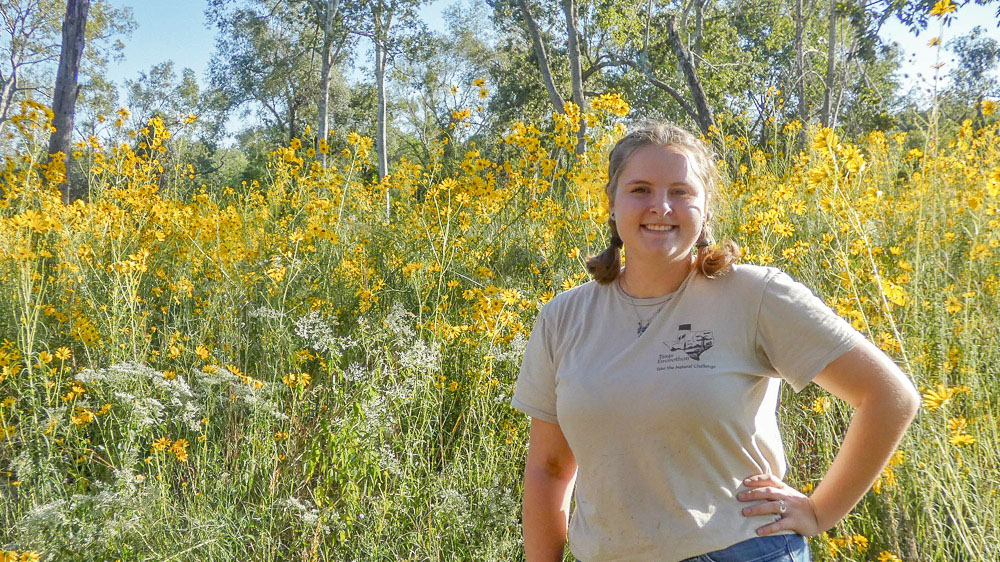 A person stands in front of a field of tall yellow flowers.