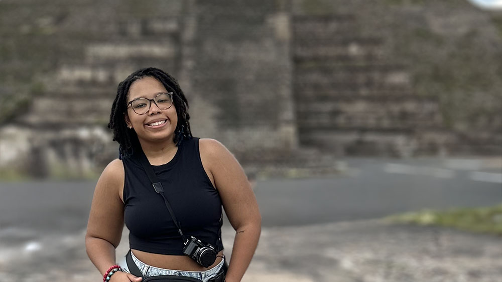 A person smiling at the camera with a blurred pyramid in the background.