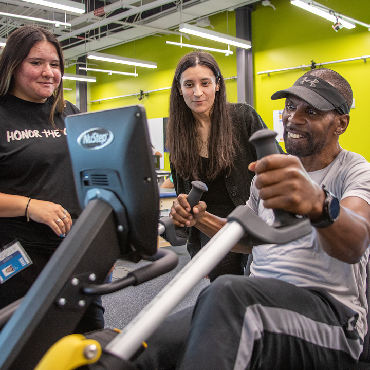 Image a person on an excerise bike with two UHCL specialists in the background